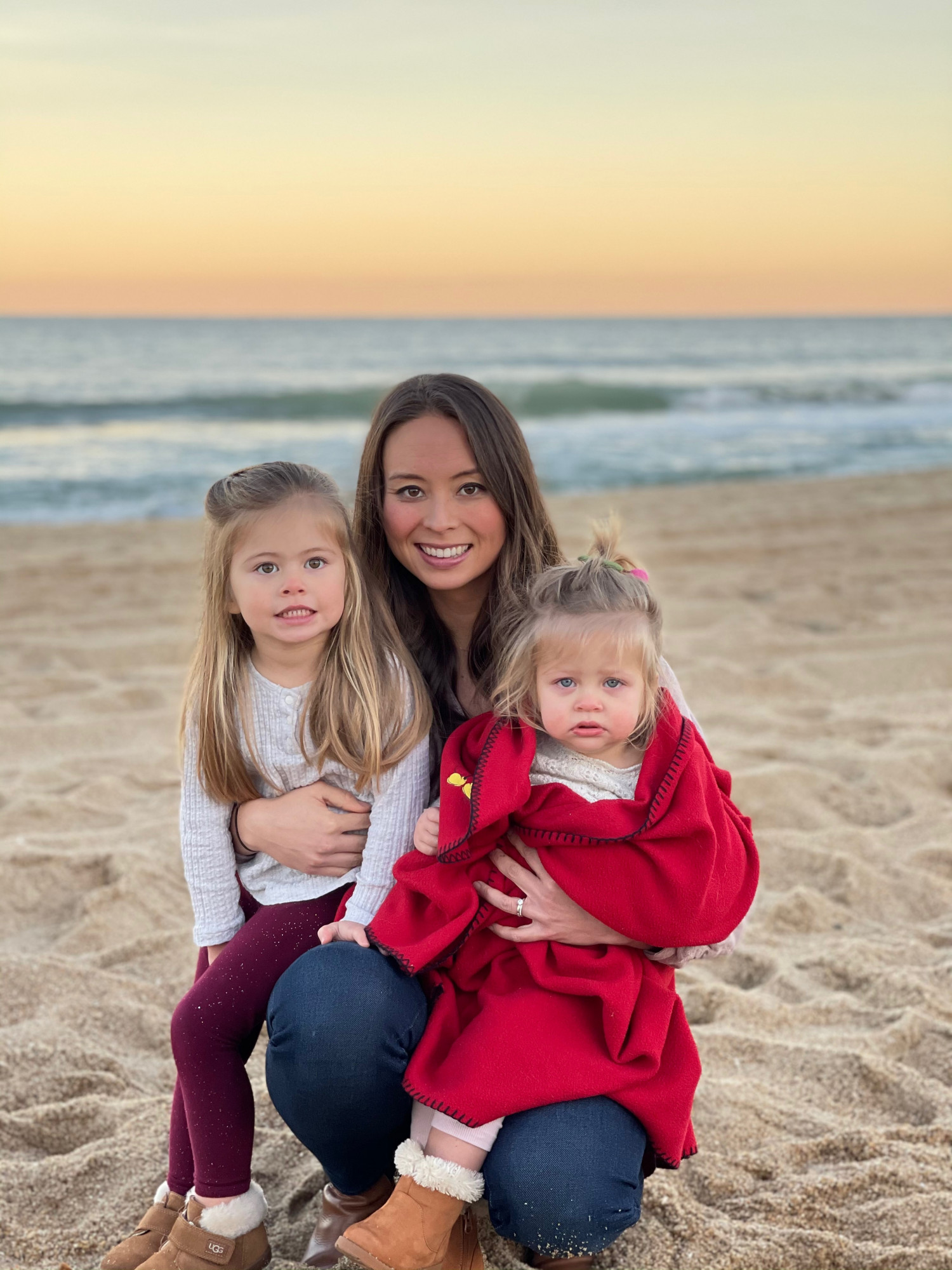 mom holding two young daughters on beach